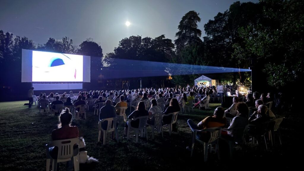 Proiezione a Parco Raggio di una serata di Concorto 2024, il pubblico è ripreso alle spalle, sullo sfondo lo schermo, sulla destra il fascio di luce della cabina di proiezione